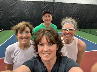 Group selfie of a PickleME207 coach and three players smiling on an indoor pickleball court.